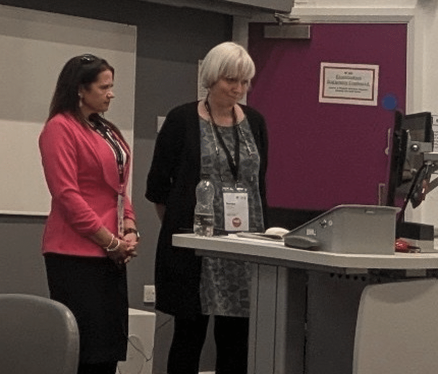 Two women at a podium with heads bowed for moment of silence