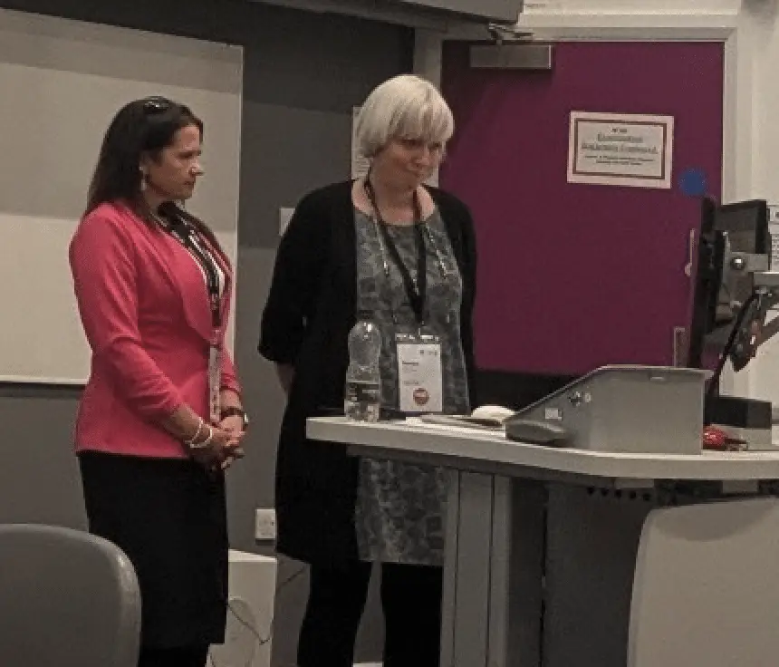Two women at a podium with heads bowed for moment of silence