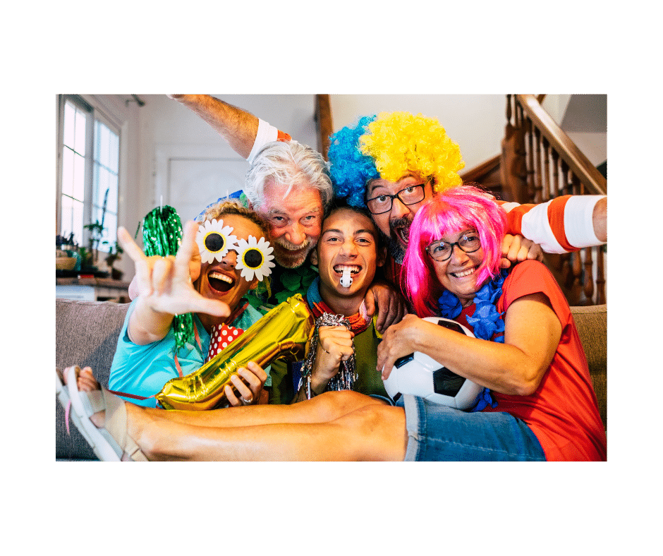 A group of people on a couch all wearing silly coloured wigs and sunglassses and holding a ball and other party items