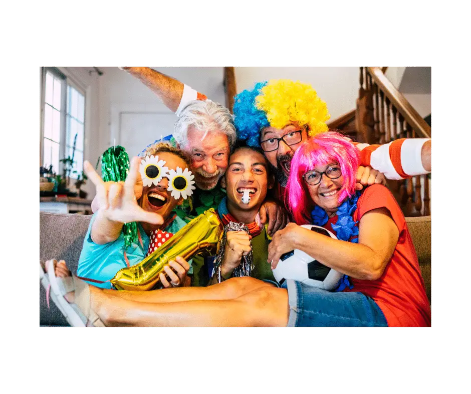 A group of people on a couch all wearing silly coloured wigs and sunglassses and holding a ball and other party items