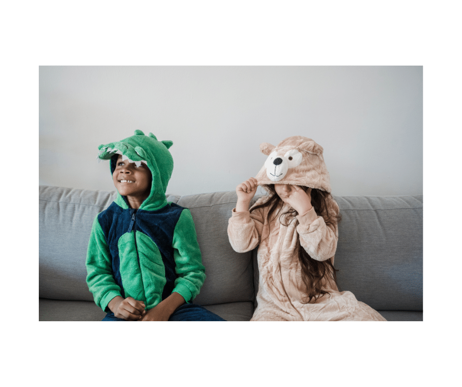 two children in pyjamas with hoods, one smiling young face peers out from a dinosaur and the other is a bear