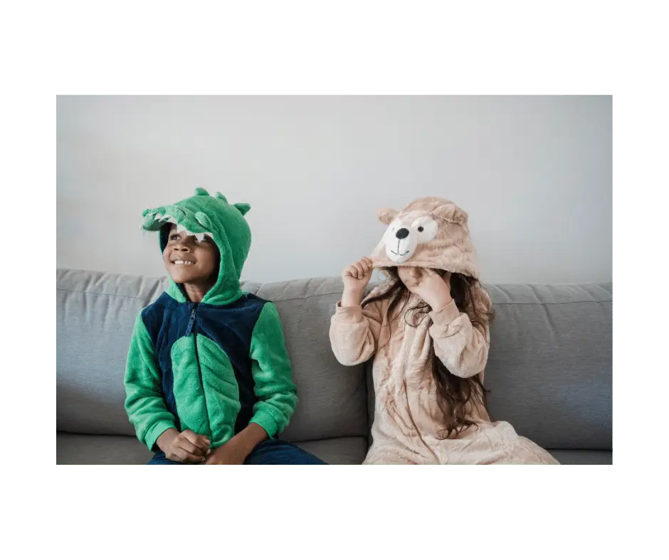 two children in pyjamas with hoods, one smiling young face peers out from a dinosaur and the other is a bear