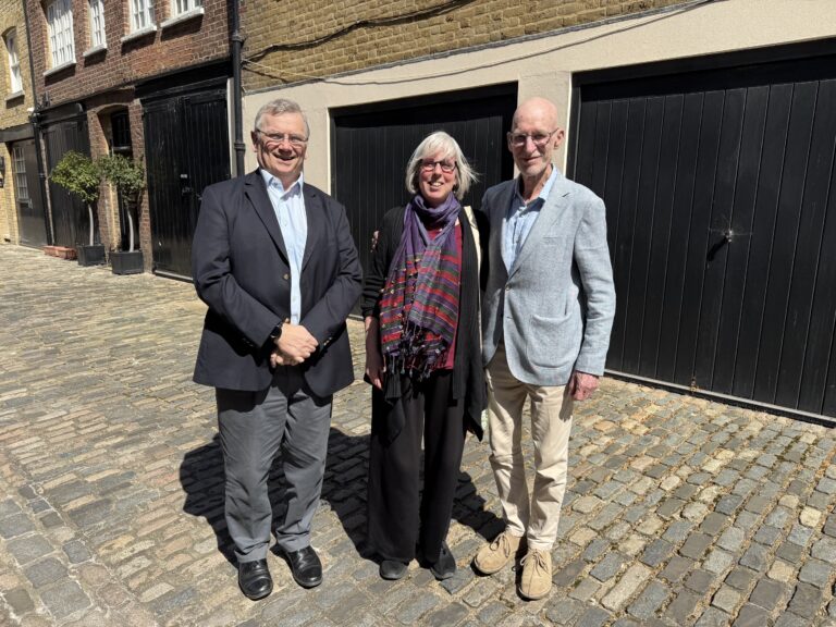 Three people outside on a sunny day, standing in front of a building and dark garage doors.