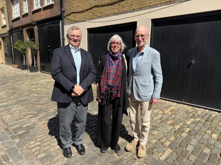 Three people outside on a sunny day, standing in front of a building and dark garage doors.